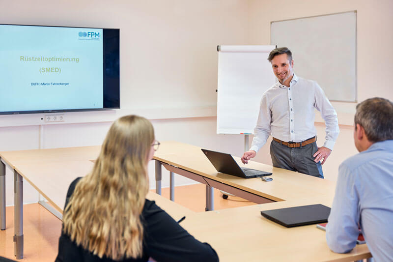 Ein Mann hält eine Präsentation vor einer Gruppe von Zuhörern in einem Konferenzraum.